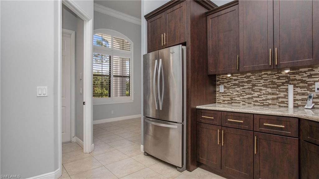 Kitchen with freestanding refrigerator, crown molding, decorative backsplash, baseboards, and light tile patterned floors