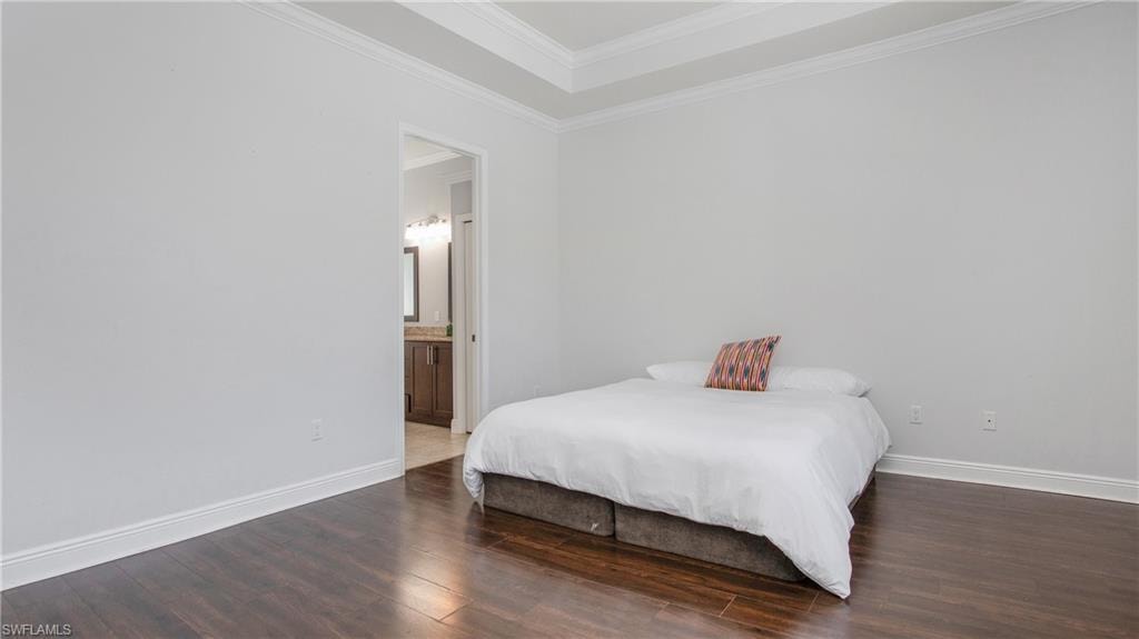 Bedroom featuring wood finished floors, ornamental molding, baseboards, and ensuite bath