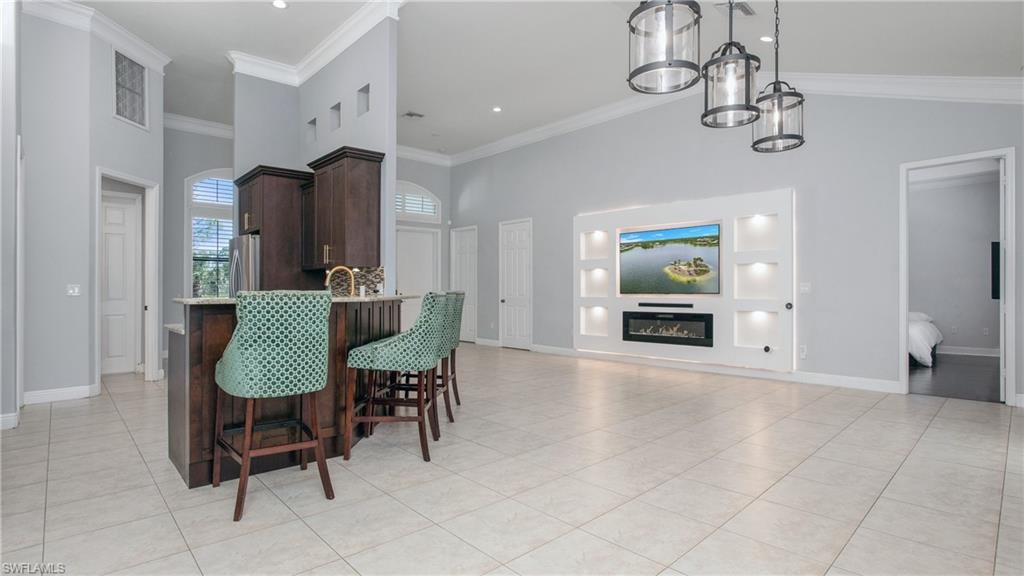 Dining room with a high ceiling, light tile patterned flooring, ornamental molding, baseboards, and a glass covered fireplace