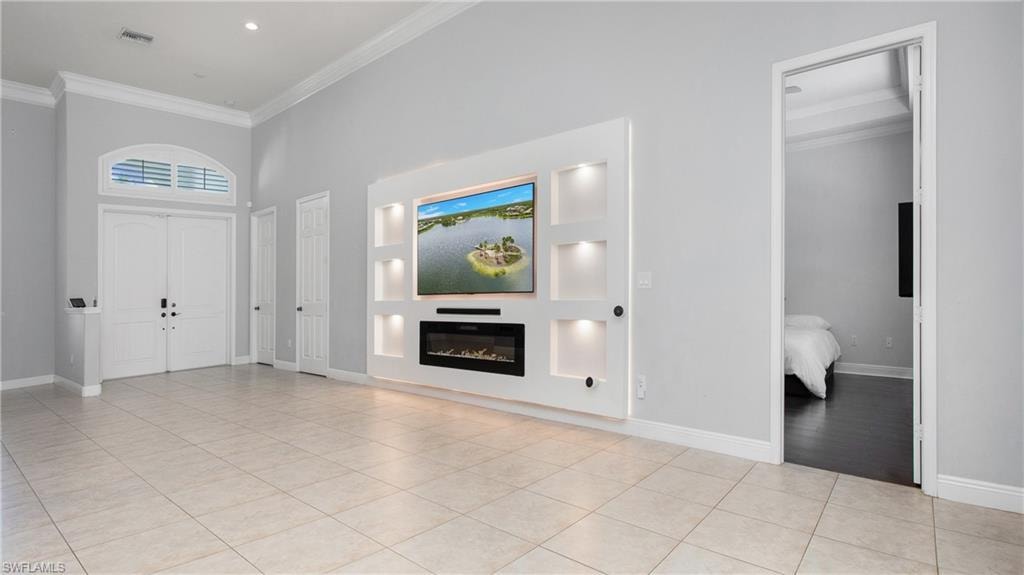Foyer featuring crown molding, light tile patterned flooring, baseboards, a glass covered fireplace, and a towering ceiling