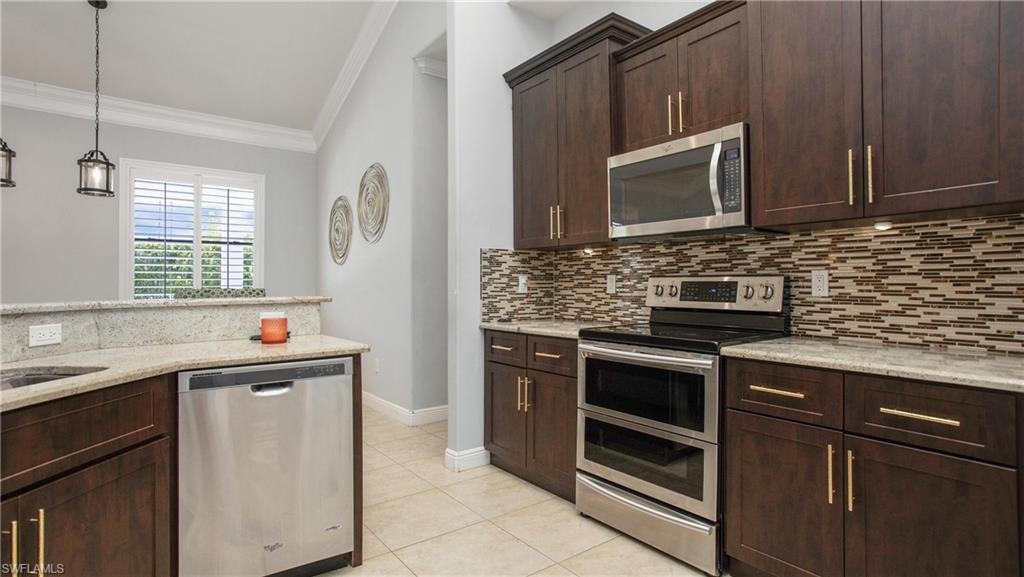 Kitchen featuring appliances with stainless steel finishes, ornamental molding, backsplash, light tile patterned floors, and dark brown cabinetry
