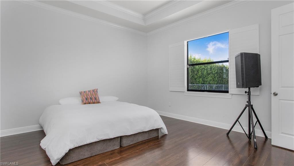 Bedroom with wood finished floors, ornamental molding, baseboards, and a tray ceiling