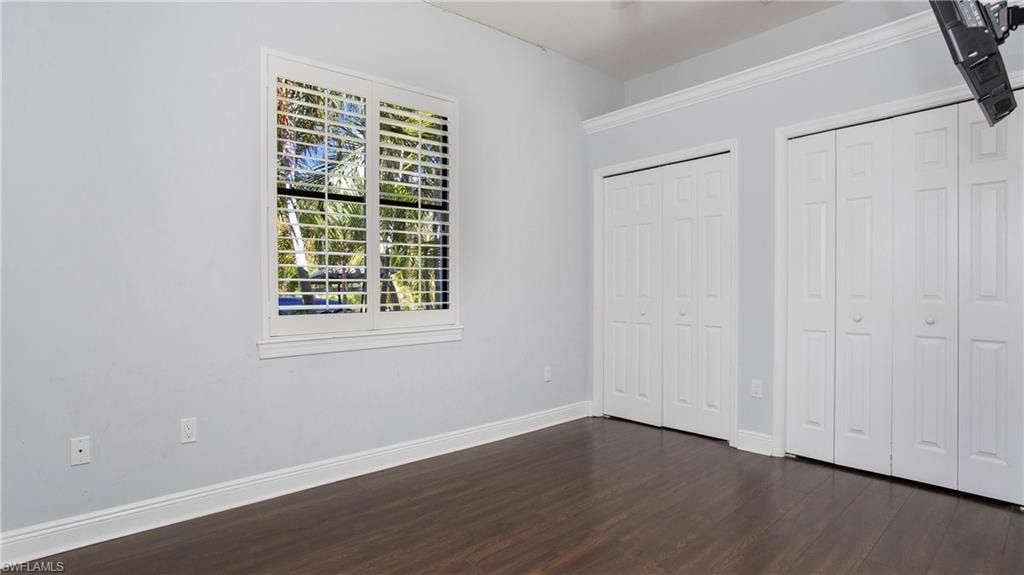 Unfurnished bedroom with dark wood-style floors, two closets, and baseboards