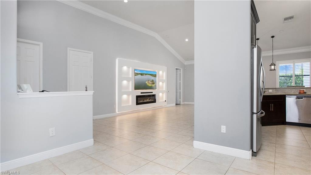 Unfurnished living room featuring light tile patterned flooring, crown molding, baseboards, a glass covered fireplace, and high vaulted ceiling