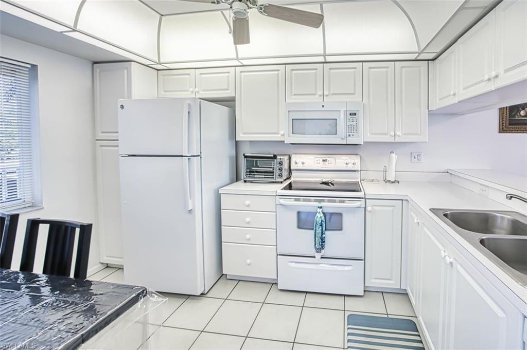 Kitchen with white cabinets, light tile patterned flooring, a sink, and white appliances