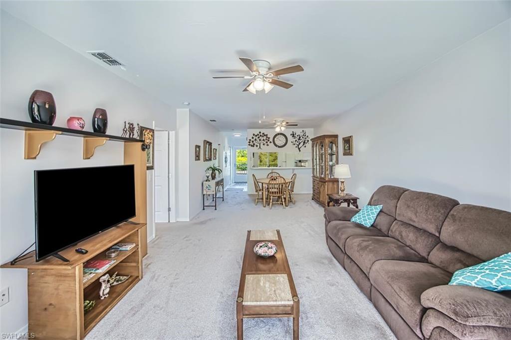 Carpeted living room with baseboards, visible vents, and ceiling fan