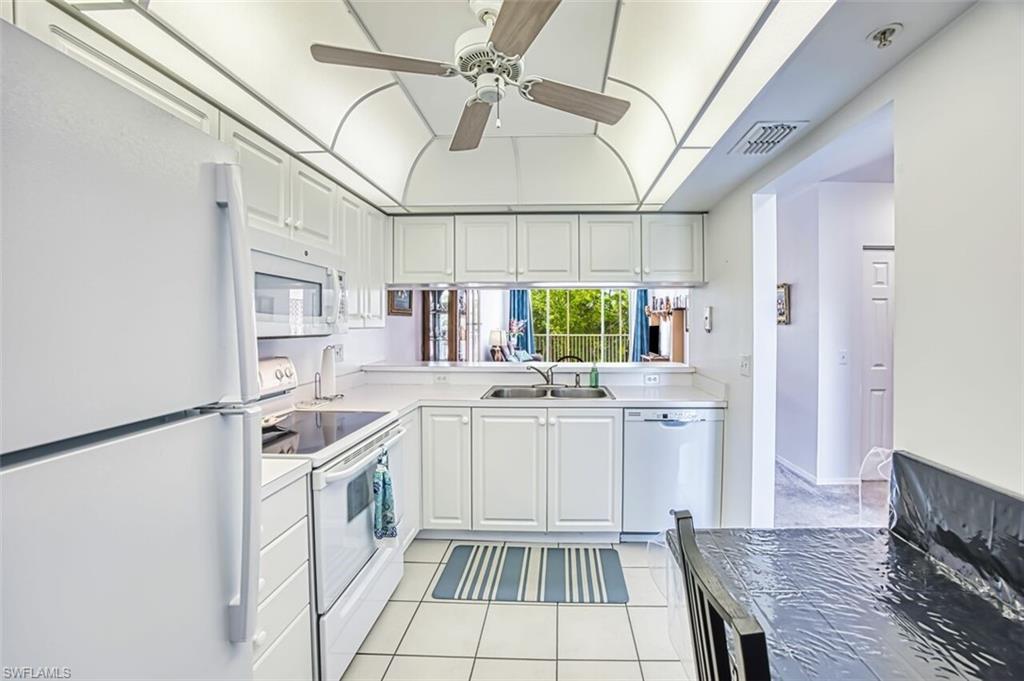 Kitchen with visible vents, a sink, light tile patterned flooring, white appliances, and ceiling fan