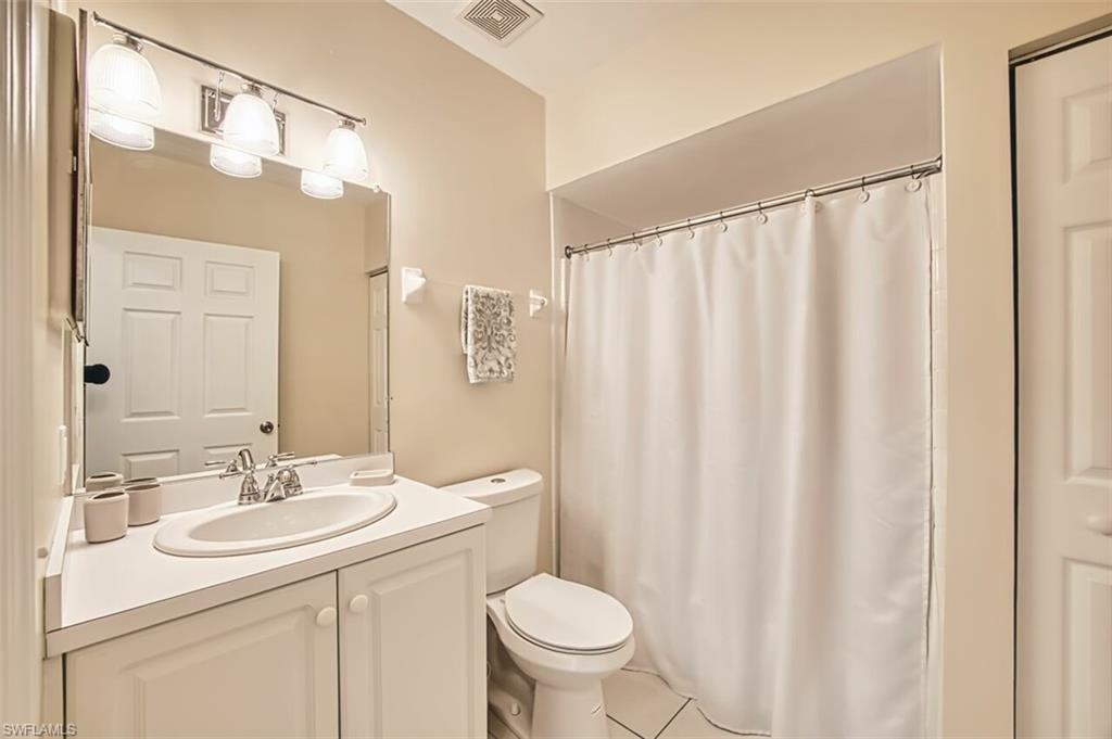 Full bathroom with tile patterned floors, toilet, visible vents, curtained shower, and vanity