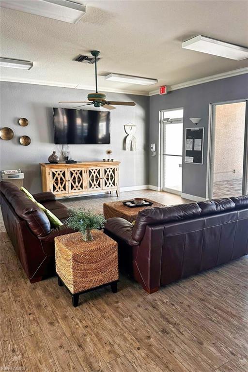 Living room featuring crown molding, wood finished floors, a textured ceiling, and a ceiling fan