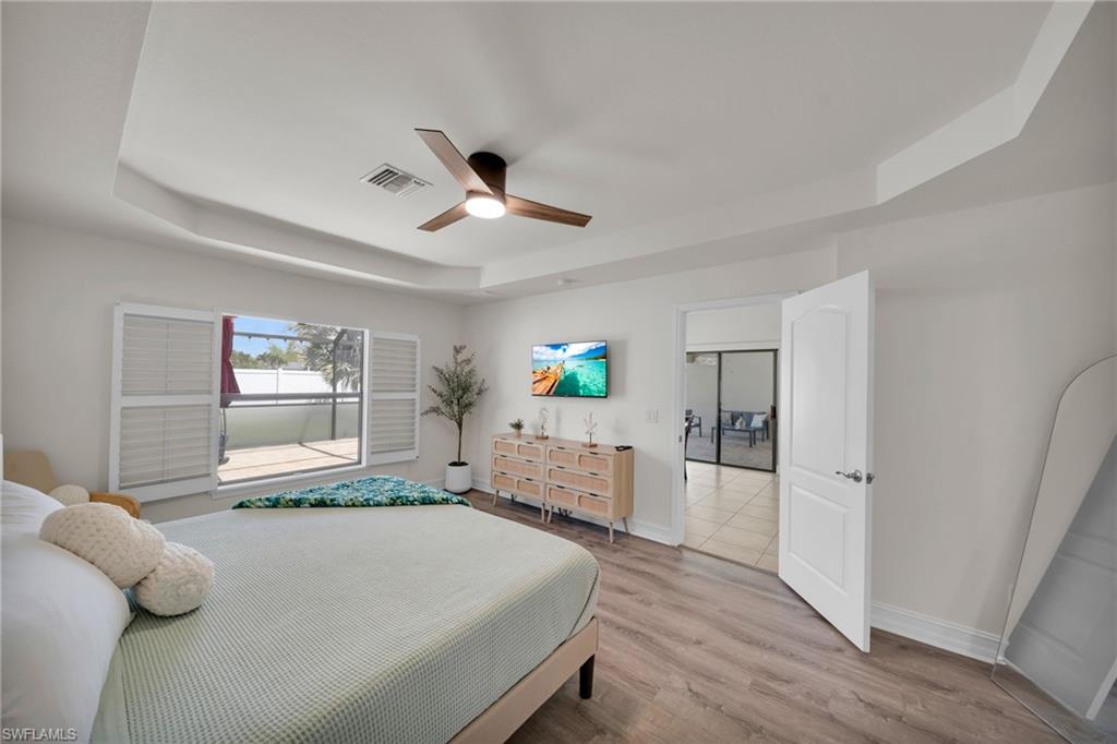 Bedroom featuring ceiling fan, a tray ceiling, visible vents, light wood-style flooring, and baseboards