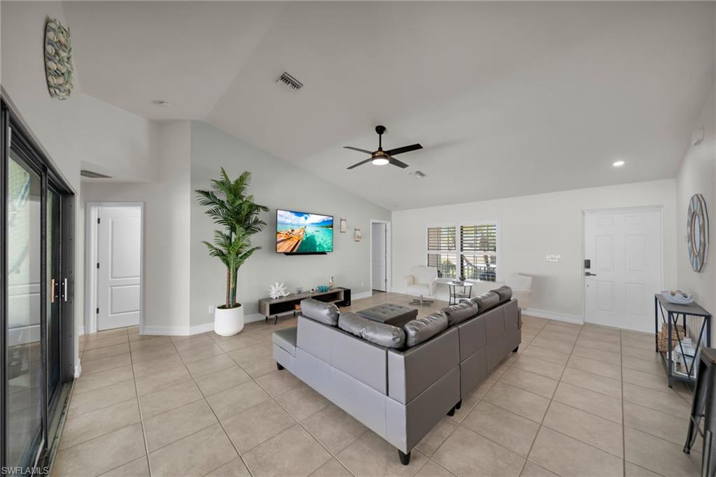 Living area with visible vents, ceiling fan, light tile patterned flooring, and lofted ceiling