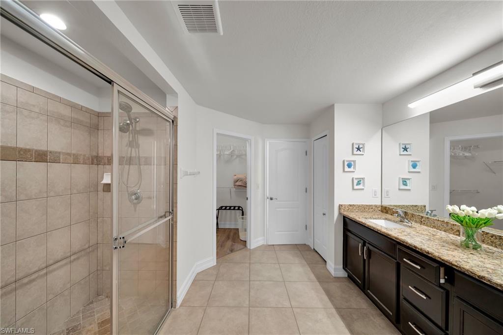Bathroom featuring visible vents, a stall shower, a spacious closet, and vanity
