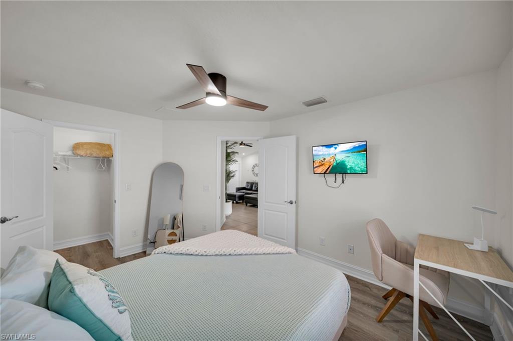 Bedroom featuring a spacious closet, wood finished floors, baseboards, visible vents, and a ceiling fan