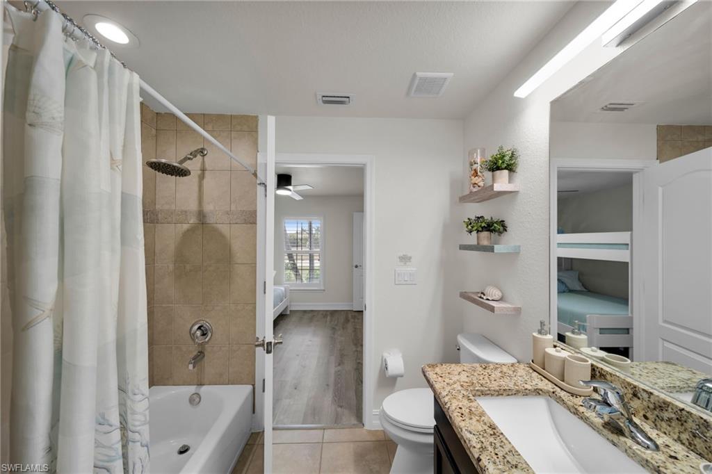 Full bathroom with shower / tub combo, visible vents, toilet, tile patterned floors, and vanity