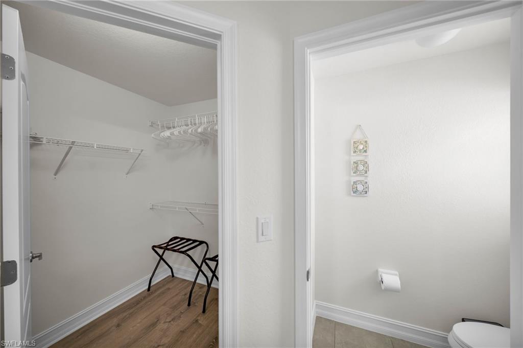 Bathroom with toilet, a spacious closet, wood finished floors, and baseboards