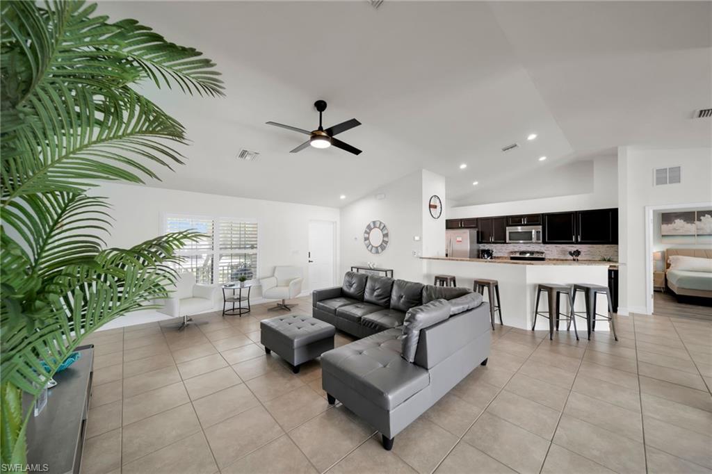Living area with light tile patterned floors, visible vents, a ceiling fan, and vaulted ceiling