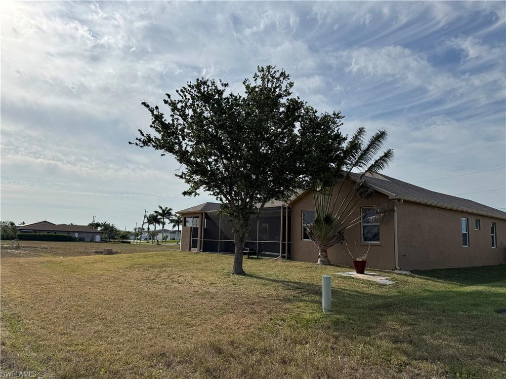 View of side of home with stucco siding, driveway, central air condition unit, and a yard
