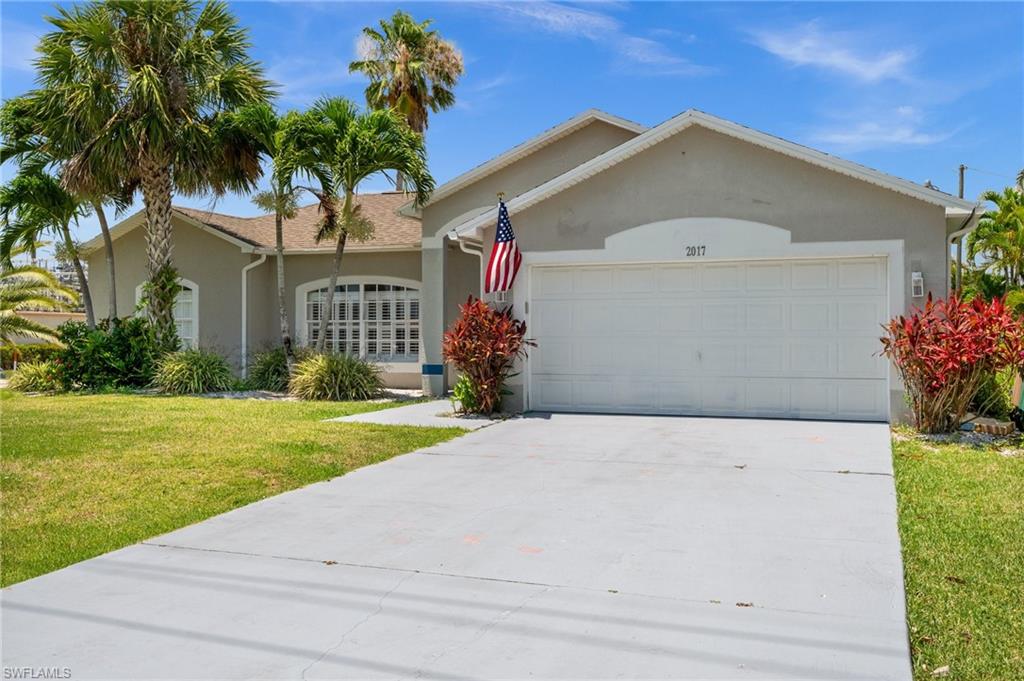 Ranch-style house featuring a garage, a front yard, stucco siding, and driveway