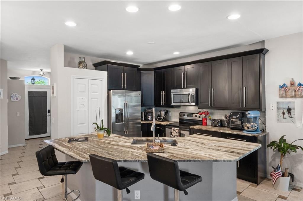 Kitchen featuring appliances with stainless steel finishes, a kitchen bar, light stone countertops, backsplash, and recessed lighting