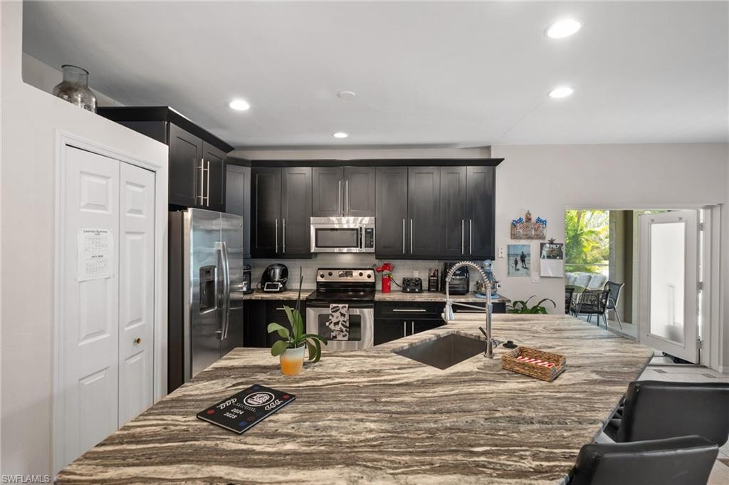 Kitchen with appliances with stainless steel finishes, a sink, recessed lighting, light stone countertops, and tasteful backsplash