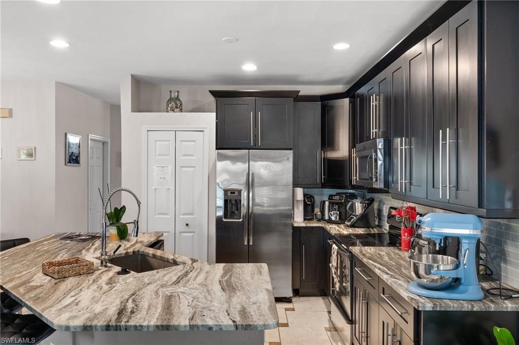 Kitchen featuring appliances with stainless steel finishes, a sink, light stone countertops, decorative backsplash, and a kitchen island with sink