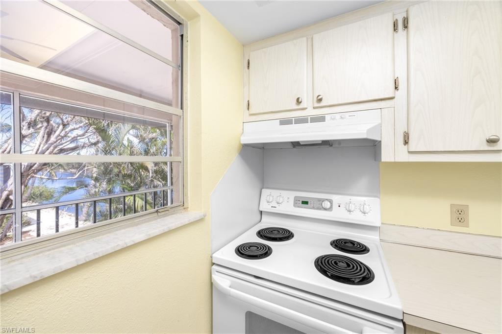 Kitchen featuring white electric stove, a wealth of natural light, and under cabinet range hood
