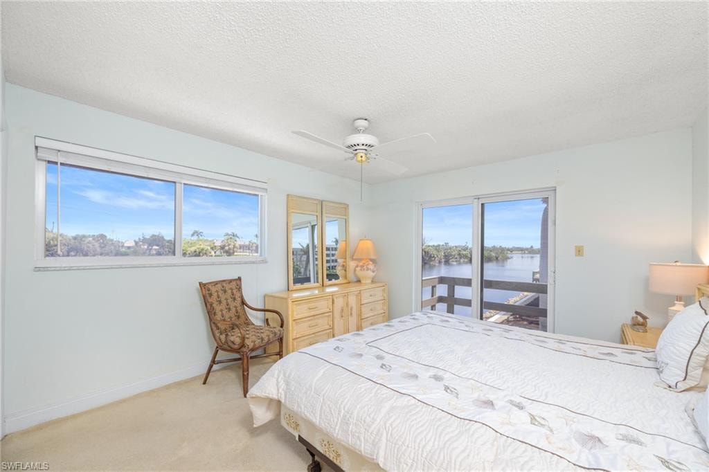 Bedroom featuring a water view, access to exterior, light carpet, baseboards, and ceiling fan