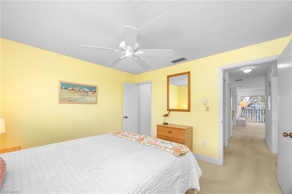 Bedroom with light carpet, a textured ceiling, baseboards, visible vents, and ceiling fan