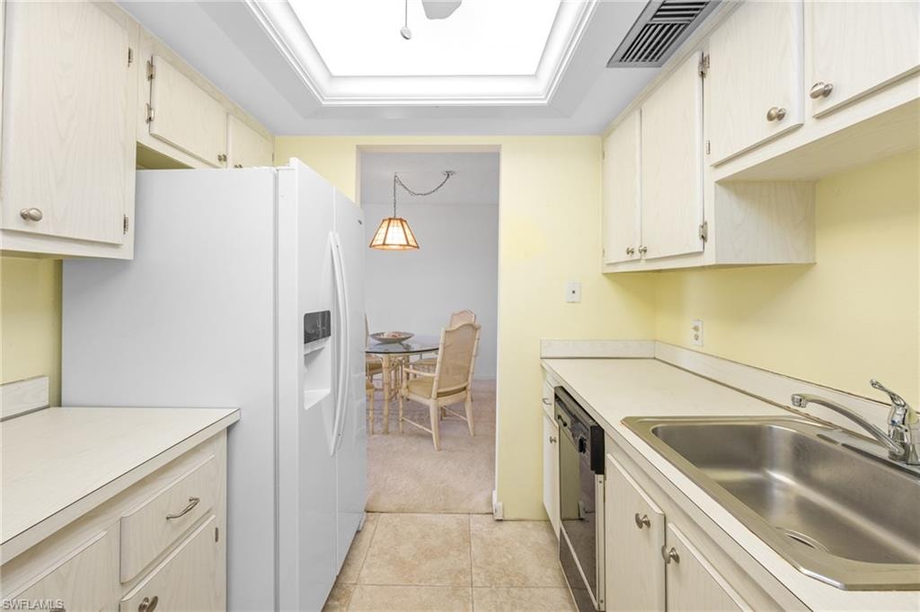 Kitchen with a sink, white refrigerator with ice dispenser, light countertops, black dishwasher, and visible vents