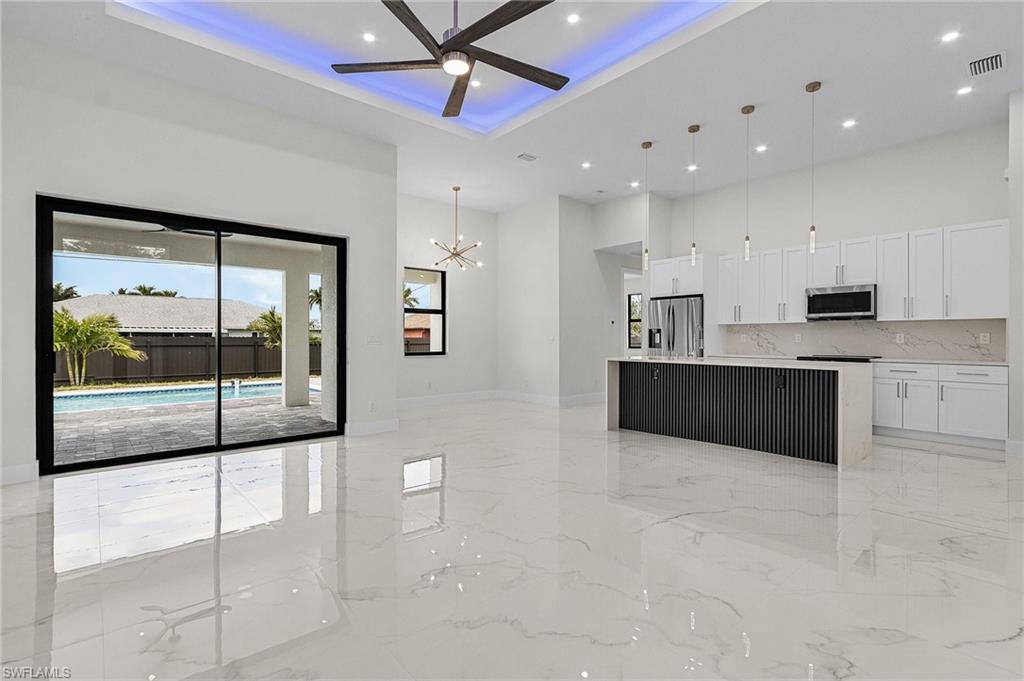 Kitchen with appliances with stainless steel finishes, porcelain floor, ceiling fan with notable chandelier, and a high ceiling