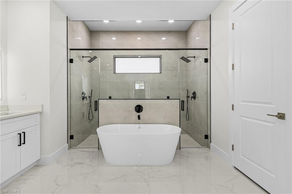Master bathroom with a stall shower, baseboards, vanity, a freestanding bath, and porcelain floors