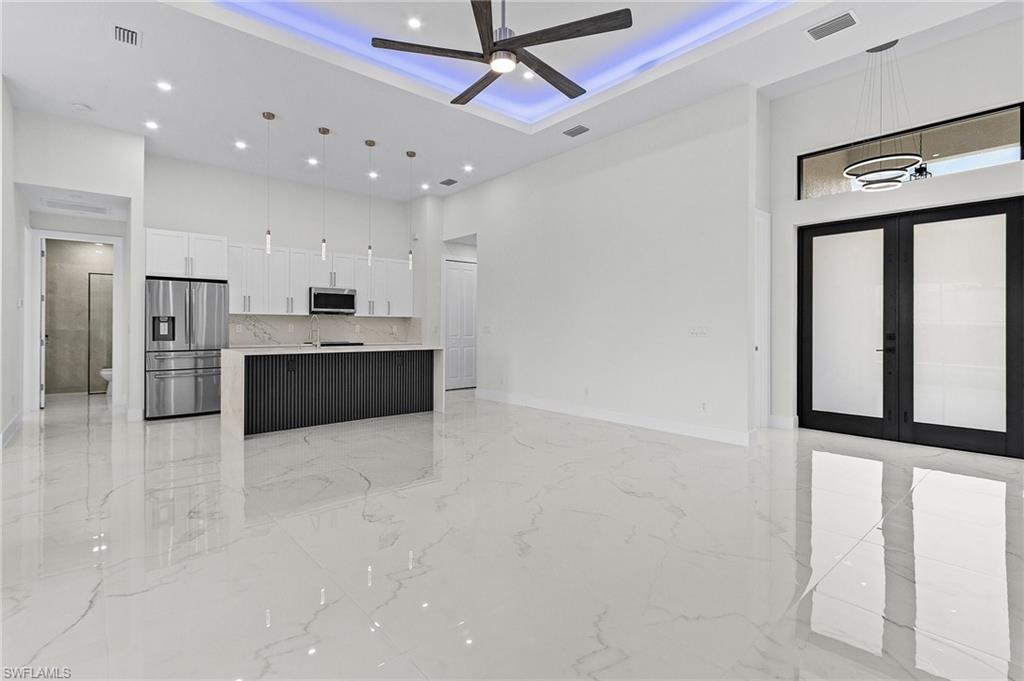 Kitchen featuring appliances with stainless steel finishes, ceiling fan, white cabinetry, open floor plan.