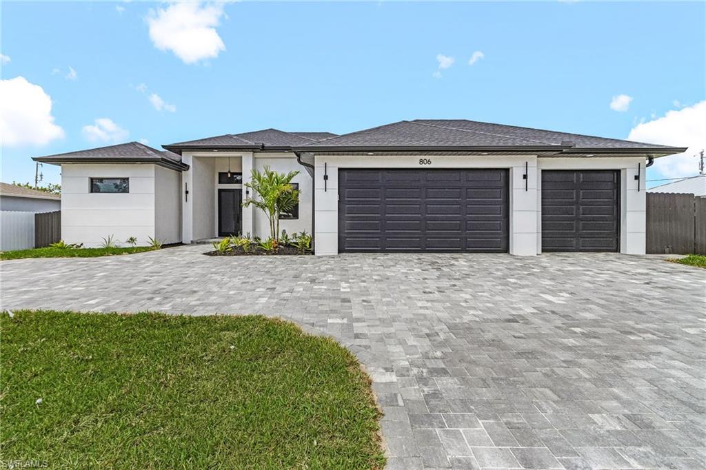 Prairie-style home with stucco siding, fence, circular driveway, an landscaped garden.