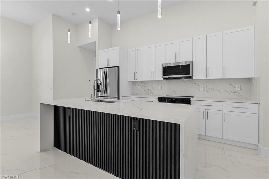 Kitchen featuring a kitchen island with sink, porcelain floors, white cabinetry, and appliances with stainless steel finishes