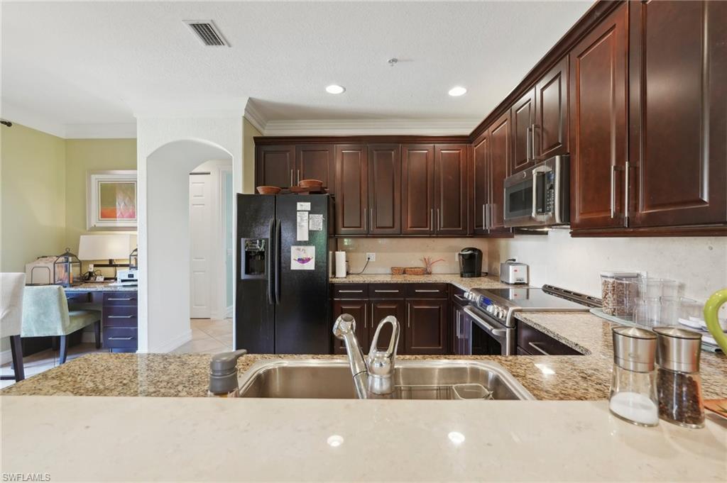 Kitchen with visible vents, arched walkways, light stone counters, a sink, and stainless steel appliances