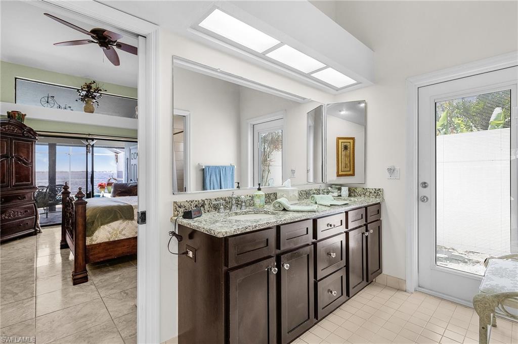 Primary ensuite Bathroom  downstairs featuring tile patterned flooring, double vanity, and exterior door to atrium and south side yard