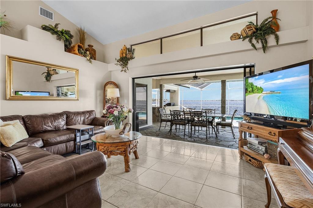 Living room with light tile patterned flooring, high vaulted ceiling, triple pocket sliders allows seamless transition to the pool and patio area for entertaining.