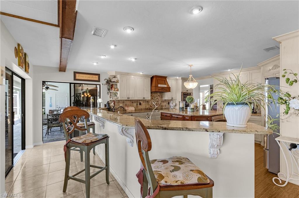Kitchen with decorative tile backsplash, a breakfast bar area, and custom exhaust hood and 2 sets of sliders to the lanai area