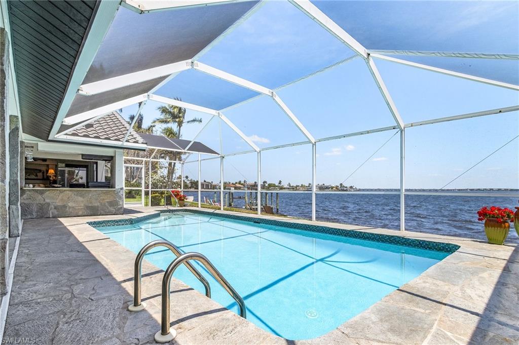 Pool with screen enclosure, a River view, and a patio area and outdoor counter and cabinets