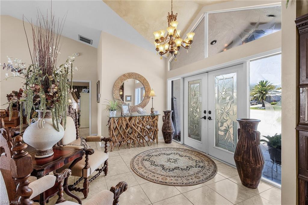 Tiled entryway featuring an inviting chandelier, high vaulted ceiling, french doors, and volumes of natural light