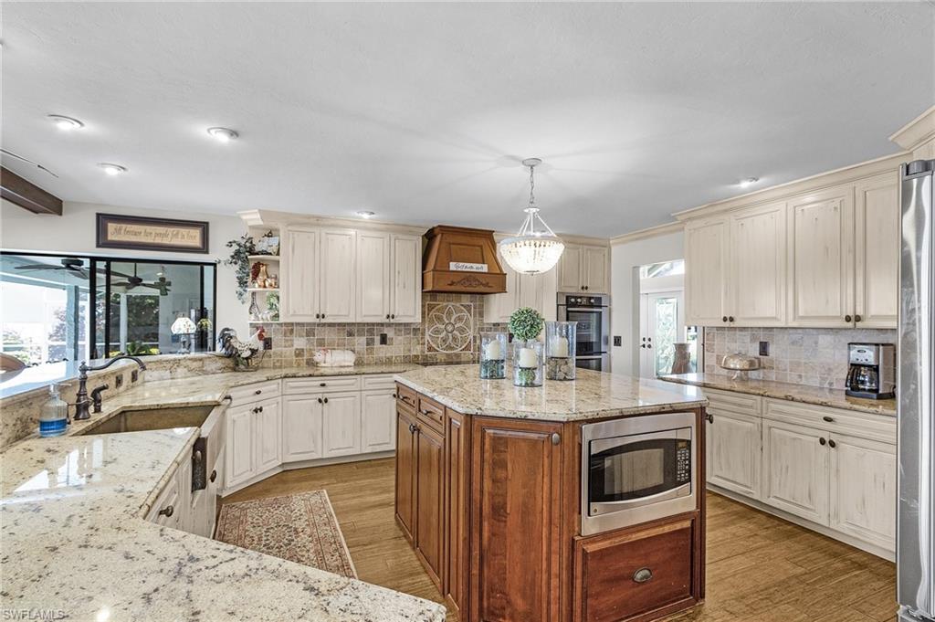 Kitchen with open decorative tile backsplash, appliances with stainless steel finishes, and light engineered wood durable flooring, and grand island