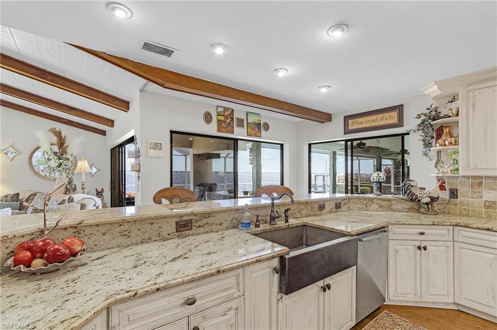 Kitchen with stainless steel dishwasher, open shelves, visible vents, granite countertops, and a copper farmers sink and huge breakfast bar