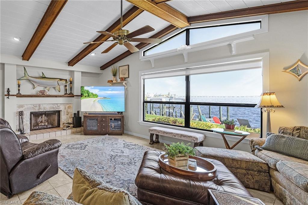 Gathering area with River view  featuring a stone wood burning fireplace, tile patterned floors, ceiling fan, and lofted ceiling with beams and the Tarpon caught from the back dock