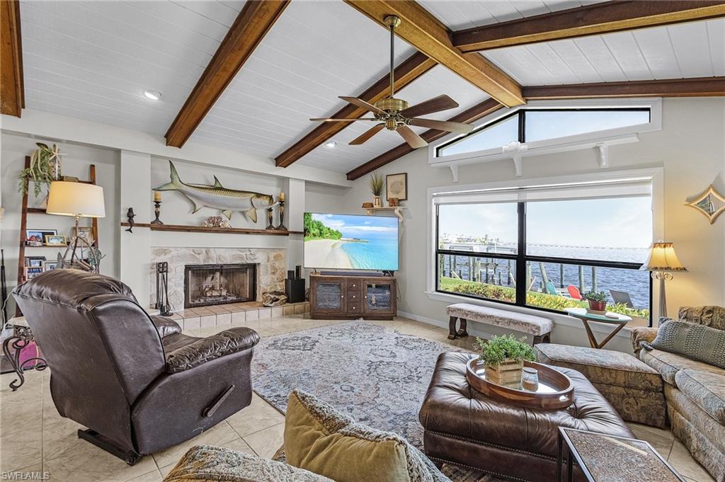Family room featuring light tile patterned flooring, ceiling fan, vaulted ceiling with beams, wood ceiling, and a stone fireplace with sliders to the pool area