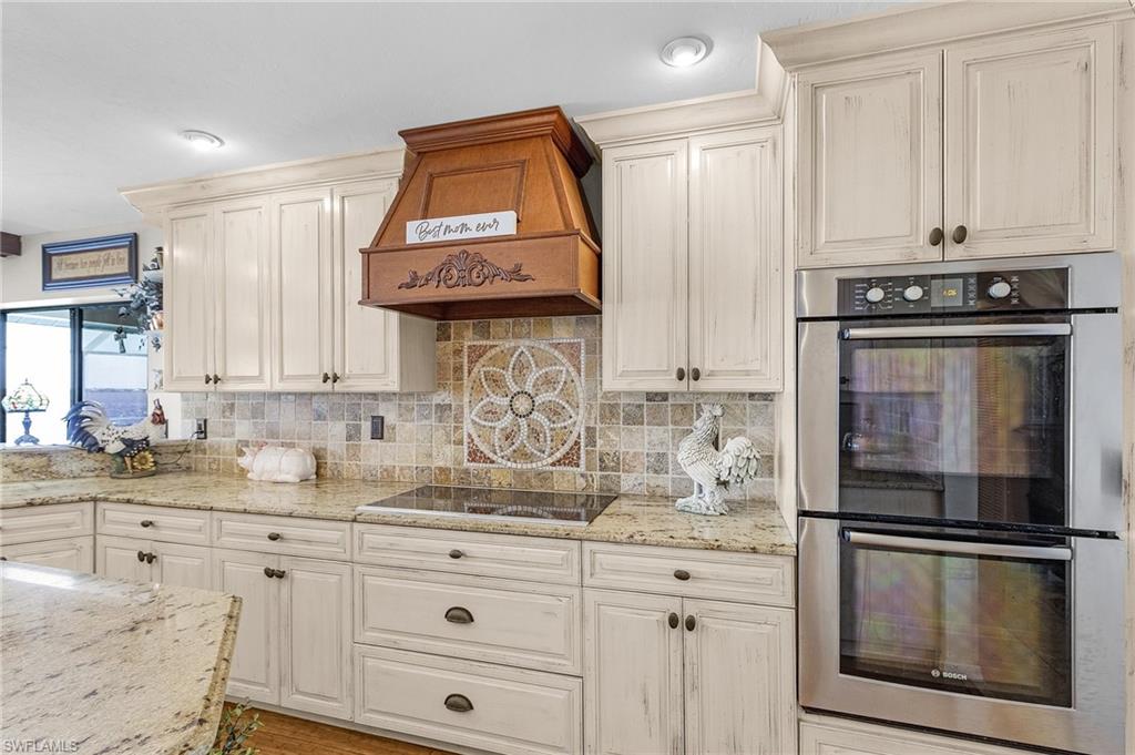 Kitchen featuring decorative tile backsplash, stainless steel double oven(convection and standard), granite countertops, premium range hood, and black electric 5 burner cook surface. Silent close drawers.
