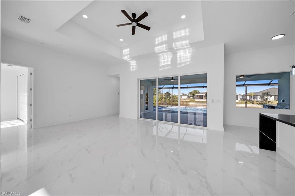 Unfurnished living room with ceiling fan, visible vents, a raised ceiling, marble finish floor, and recessed lighting