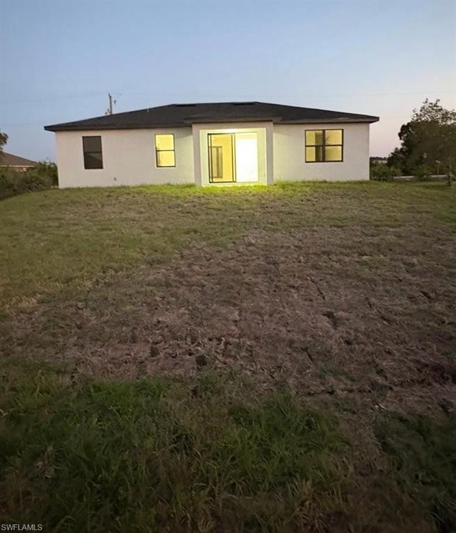 Back of house with stucco siding and a lawn
