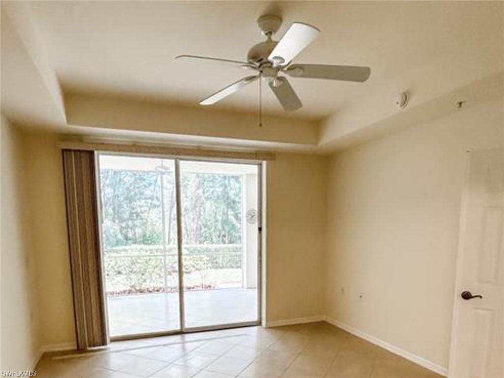 Empty room with baseboards, a ceiling fan, a tray ceiling, and light tile patterned floors
