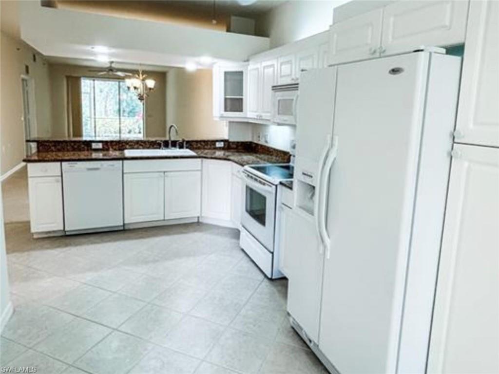 Kitchen with a sink, white cabinetry, dark countertops, and white appliances