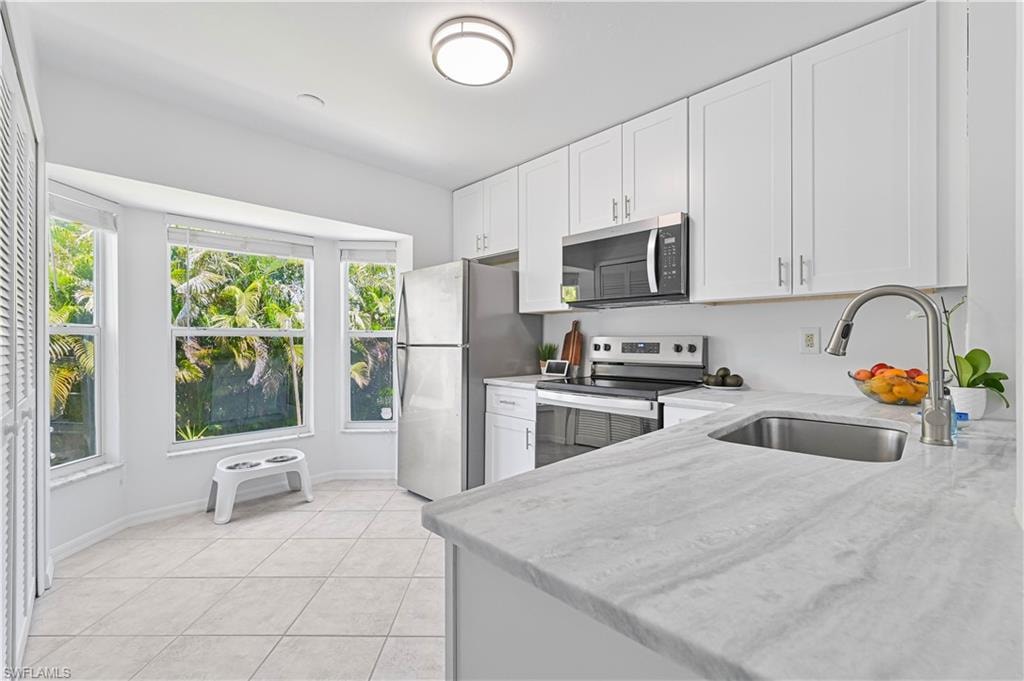 Kitchen featuring light stone countertops, baseboards, white cabinetry, a sink, and stainless steel appliances